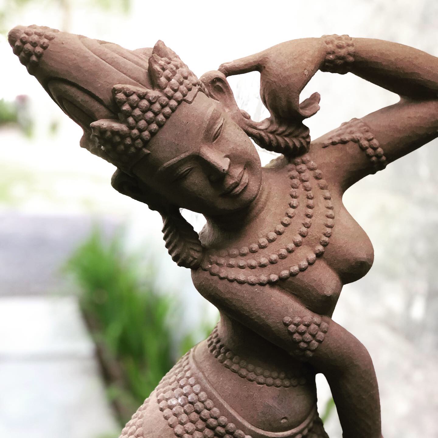 “Cambodian Khmer Apsara Dancer with her left arm raised in a dynamic dancing pose, wearing a headdress and a garland”, Amansara Angkor